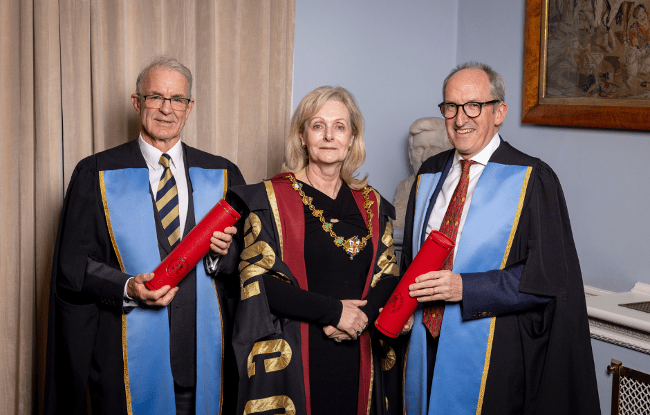 Mike McKirdy stands on the right holding his Diploma, with Professor Laura Viani and Hon Fellow John Matheson